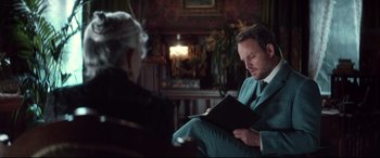 Movie still from “Winchester” (2018), directed by Michael Spierig – A man sitting in a chair reading a book to a woman; Medium shot, Over the shoulder angle