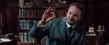 Movie still from “Winchester” (2018), directed by Michael Spierig – A man wearing a suit and tie in a room with books; Close Up shot, Low angle