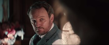 Movie still from “Winchester” (2018), directed by Michael Spierig – A person wearing a suit and tie; Close Up shot, Over the shoulder angle