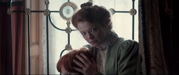 Movie still from “Winchester” (2018), directed by Michael Spierig – A woman holding a red haired doll in front of a window; Close Up shot, Over the shoulder angle
