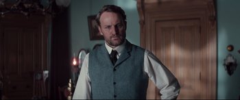 Movie still from “Winchester” (2018), directed by Michael Spierig – A man in a vest and tie standing in front of a mirror; Medium shot, Low angle