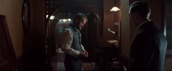 Movie still from “Winchester” (2018), directed by Michael Spierig – A man standing in a room looking at his watch; Medium shot, Low angle