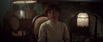 Movie still from “Winchester” (2018), directed by Michael Spierig – A young boy sitting in a chair in front of a fire place; Medium shot, Over the shoulder angle