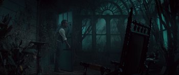 Movie still from “Winchester” (2018), directed by Michael Spierig – A man standing next to a door in a dark room; Wide shot, Over the shoulder angle