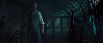 Movie still from “Winchester” (2018), directed by Michael Spierig – A man standing in front of a window in a dark room; Medium shot, Low angle