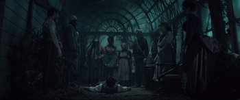 Movie still from “Winchester” (2018), directed by Michael Spierig – A group of people standing around a man laying on the ground; Wide shot, High angle
