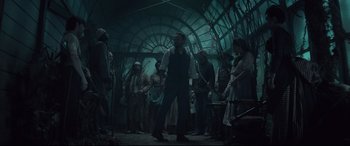 Movie still from “Winchester” (2018), directed by Michael Spierig – A group of people standing around in a room; Wide shot, Low angle