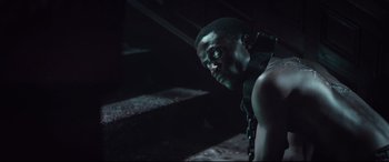 Movie still from “Winchester” (2018), directed by Michael Spierig – A man with a chain around his neck looking at the camera; Close Up shot, Over the shoulder angle