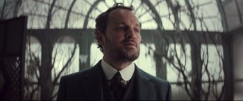 Movie still from “Winchester” (2018), directed by Michael Spierig – A man wearing a suit and tie in front of a window; Close Up shot, Low angle