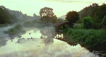 Movie still from “Winged Migration” (2001), directed by Jacques Cluzaud – A lake with a boat dock and a boat house; Extreme Wide shot, Low angle