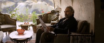 Movie still from “Winter Sleep” (2014), directed by Nuri Bilge Ceylan – A man sitting in a chair holding a newspaper; Medium shot, Low angle