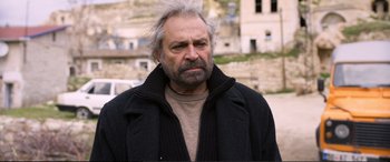 Movie still from “Winter Sleep” (2014), directed by Nuri Bilge Ceylan – An older man with a gray beard wearing a black jacket; Close Up shot, Over the shoulder angle