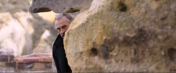Movie still from “Winter Sleep” (2014), directed by Nuri Bilge Ceylan – An older man looking at the camera from behind a rock wall; Medium shot, Low angle