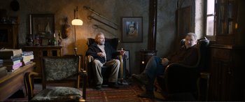 Movie still from “Winter Sleep” (2014), directed by Nuri Bilge Ceylan – A man sitting in a chair in front of a painting; Wide shot, Over the shoulder angle