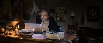 Movie still from “Winter Sleep” (2014), directed by Nuri Bilge Ceylan – A man sitting in front of a bunch of books on a table; Medium shot, High angle