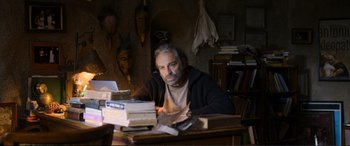 Movie still from “Winter Sleep” (2014), directed by Nuri Bilge Ceylan – A man sitting at a desk with a stack of books; Medium shot, Low angle