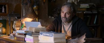 Movie still from “Winter Sleep” (2014), directed by Nuri Bilge Ceylan – An older man sitting in front of a stack of books; Medium shot, Over the shoulder angle