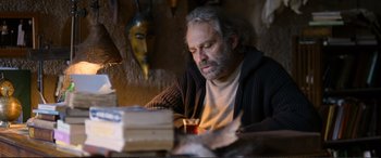 Movie still from “Winter Sleep” (2014), directed by Nuri Bilge Ceylan – An older man sitting in front of a stack of books; Medium shot, Low angle