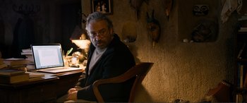Movie still from “Winter Sleep” (2014), directed by Nuri Bilge Ceylan – A man sitting at a table in front of a wall with a lot of trophies on the wall; Medium shot, Over the shoulder angle