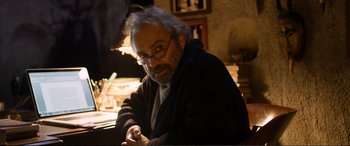 An older man sitting at a table in front of a lamp