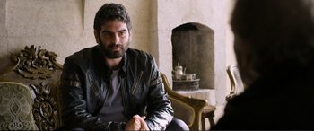 Movie still from “Winter Sleep” (2014), directed by Nuri Bilge Ceylan – A man sitting in a chair wearing a leather jacket; Medium shot, Over the shoulder angle