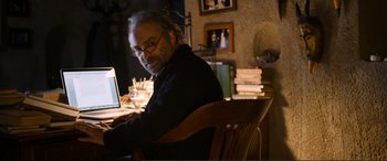 Movie still from “Winter Sleep” (2014), directed by Nuri Bilge Ceylan – A man sitting in front of a laptop computer on top of a wooden table; Medium shot, Low angle