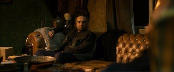 Movie still from “Winter Sleep” (2014), directed by Nuri Bilge Ceylan – A man sitting on top of a couch in a living room; Medium shot, Over the shoulder angle