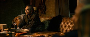 Movie still from “Winter Sleep” (2014), directed by Nuri Bilge Ceylan – A man sitting on top of a couch next to pillows; Medium shot, Over the shoulder angle