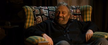 Movie still from “Winter Sleep” (2014), directed by Nuri Bilge Ceylan – An older man sitting on a couch smiling; Medium shot, High angle