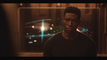 Movie still from “Another Life” (2019), created by Aaron Martin – A man standing in front of an image of a space station; Close Up shot, Low angle