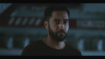 Movie still from “Another Life” (2019), created by Aaron Martin – A person wearing a black shirt; Close Up shot, Over the shoulder angle
