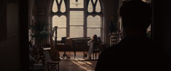 Movie still from “Winter's Tale” (2014), directed by Akiva Goldsman – A woman sitting in front of a piano in front of a large window; Wide shot, High angle