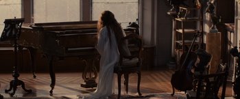 Movie still from “Winter's Tale” (2014), directed by Akiva Goldsman – A woman sitting in front of a piano in front of a window; Wide shot, High angle