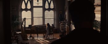 Movie still from “Winter's Tale” (2014), directed by Akiva Goldsman – A woman sitting in front of a grand piano in a living room; Wide shot, Over the shoulder angle