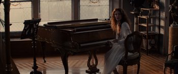 Movie still from “Winter's Tale” (2014), directed by Akiva Goldsman – A woman sitting in front of a piano in front of a window; Wide shot, High angle