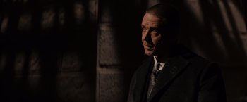 Movie still from “Winter's Tale” (2014), directed by Akiva Goldsman – A man wearing a suit and tie standing in the dark; Close Up shot, Over the shoulder angle
