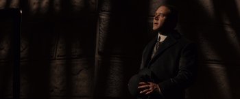 Movie still from “Winter's Tale” (2014), directed by Akiva Goldsman – A man in a suit and tie holding a hat; Medium shot, Low angle