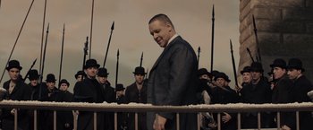Movie still from “Winter's Tale” (2014), directed by Akiva Goldsman – A man in a suit standing in front of a group of men; Medium shot, Low angle