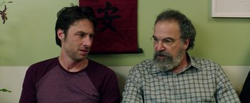 Movie still from “Wish I Was Here” (2014), directed by Zach Braff – Two men sitting next to each other in front of a painting; Close Up shot, Over the shoulder angle