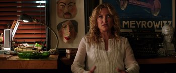 Movie still from “Wish I Was Here” (2014), directed by Zach Braff – A woman standing in front of a wall with masks on it; Close Up shot, Over the shoulder angle