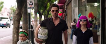 Movie still from “Wish I Was Here” (2014), directed by Zach Braff – A man walking down the street holding a jar of money; Medium shot, Over the shoulder angle