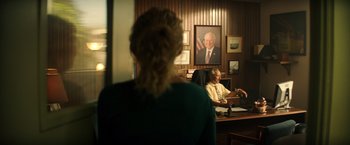 Movie still from “Wish I Was Here” (2014), directed by Zach Braff – Two people sitting at a desk in front of a painting; Medium shot, Over the shoulder angle