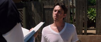 Movie still from “Wish I Was Here” (2014), directed by Zach Braff – A man in a white t - shirt is holding a book; Close Up shot, Over the shoulder angle