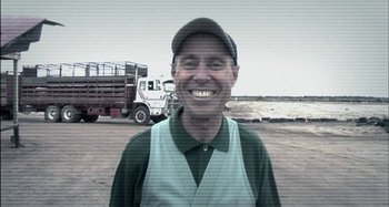 Movie still from “Wolf Creek” (2005), directed by Greg McLean – A man wearing a cap and vest standing in front of a truck; Medium shot, Low angle