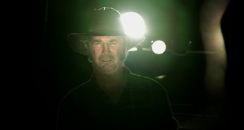Movie still from “Wolf Creek” (2005), directed by Greg McLean – A man wearing a hat standing in front of a street light at night; Close Up shot, Low angle
