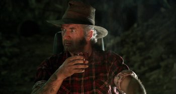 Movie still from “Wolf Creek” (2005), directed by Greg McLean – An old man with a beard and a hat is holding a glass of wine; Close Up shot, Over the shoulder angle