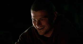 Movie still from “Wolf Creek” (2005), directed by Greg McLean – A person smiling with a dark background; Close Up shot, Low angle