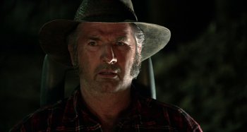 Movie still from “Wolf Creek” (2005), directed by Greg McLean – An older man wearing a cowboy hat and plaid shirt; Close Up shot, Over the shoulder angle