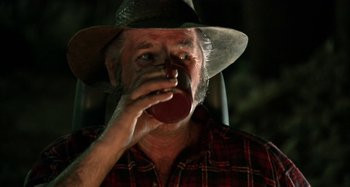 Movie still from “Wolf Creek” (2005), directed by Greg McLean – An older man wearing a cowboy hat drinking a cup of coffee; Close Up shot, Low angle