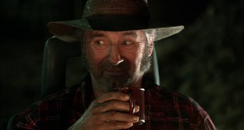 Movie still from “Wolf Creek” (2005), directed by Greg McLean – An older man wearing a cowboy hat and holding a mug; Close Up shot, Over the shoulder angle